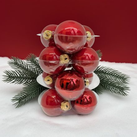 Piros üveg karácsonyi gömb szett fenyőág és havas háttér dekorációval.
