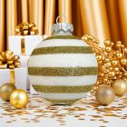 Gold Glitter Stripe fehér-arany kézzel festett üveg gömb, arany ajándékdobozok és ünnepi dekoráció előtt.