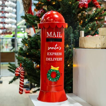 Karácsonyfa mellett elhelyezett piros fém postaláda ünnepi dekorációként.
