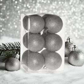 Ezüst glitteres műanyag karácsonyi gömb szett (12×6 cm) átlátszó dobozban, havas felületen, ezüst háttérrel.