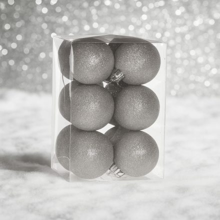 Ezüst glitteres műanyag karácsonyi gömb szett (12×6 cm) átlátszó dobozban, havas felületen, ezüst háttérrel.