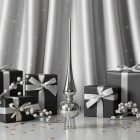 Fényes ezüstszínű üveg csúcsdísz ajándékdobozok és ezüst bogyós ágak között, elegáns ezüst háttér előtt.