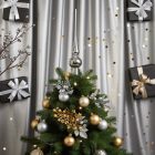 Ezüst üveg csúcsdísz karácsonyfán elhelyezve, arany és ezüst gömbökkel, fényfüzérrel és ajándékdobozos háttérrel.