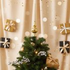 Pezsgő színű üveg csúcsdísz karácsonyfa tetején, arany és fekete ajándékdobozokkal a háttérben.