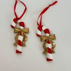 Két piros-fehér csíkos nyalóka arany masnival, piros akasztóval, fehér háttéren.