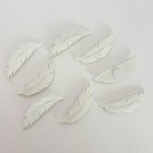 Fehér öntapadós tollfigurák fehér háttéren, egy darab hátoldala látható a ragasztókoronggal.