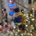 Egy diótörő katona figura különböző színekben és sapkákkal, arany akasztóval, fehér háttéren.