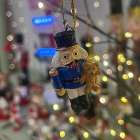 Egy diótörő katona figura különböző színekben és sapkákkal, arany akasztóval, fehér háttéren.