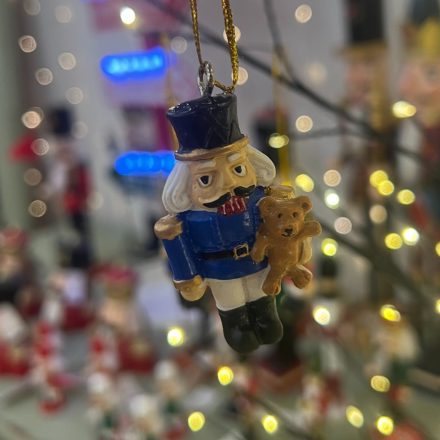 Egy diótörő katona figura különböző színekben és sapkákkal, arany akasztóval, fehér háttéren.