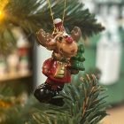 Egy rénszarvas figura piros ruhában, zöld fenyőfával és arany akasztóval