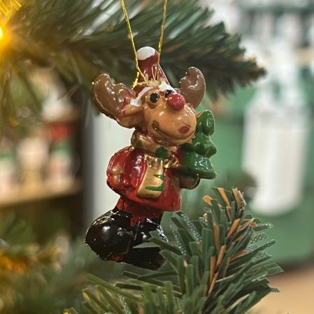 Egy rénszarvas figura piros ruhában, zöld fenyőfával és arany akasztóval