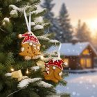 Mézeskalács gnóm díszek hófödte fenyőágon, téli tájjal és fényfüzérrel a háttérben.