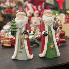 Kétféle Mikulás poly figura karácsonyi háttéren, az egyik karácsonyfával, a másik ajándékzsákkal.