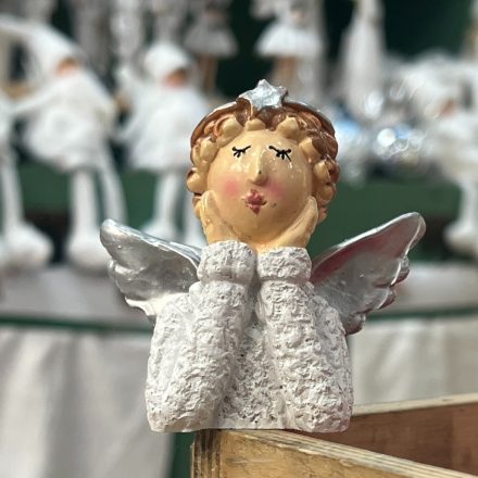 Könyöklő angyal figura fehér ruhában, ezüst szárnyakkal és arany hajjal, dekoratív háttérben
